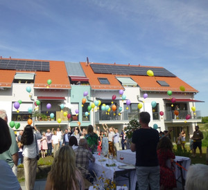 Wohngebäude mit Ziegeldach, Menschen im Vordergrund, die Luftballons steigen lassen