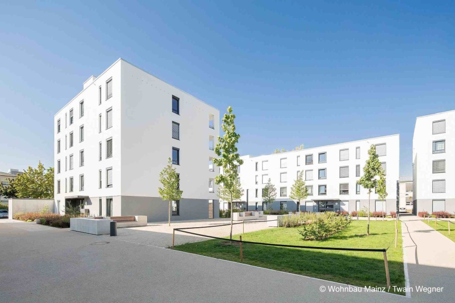 Wohngebäude des Cavalier Holstein in Mainz, weiße Fassade mit Flachdach, Grünfläche und Spielplatz im Vordergrund